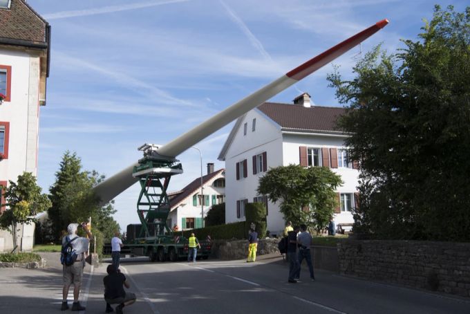 Ein Lastwagen transportiert ein Rotorblatt eines neuen Windkraftwerks durch La Ferrière im Berner Jura. Rotor Windrad Windenergie Windkraftwerk