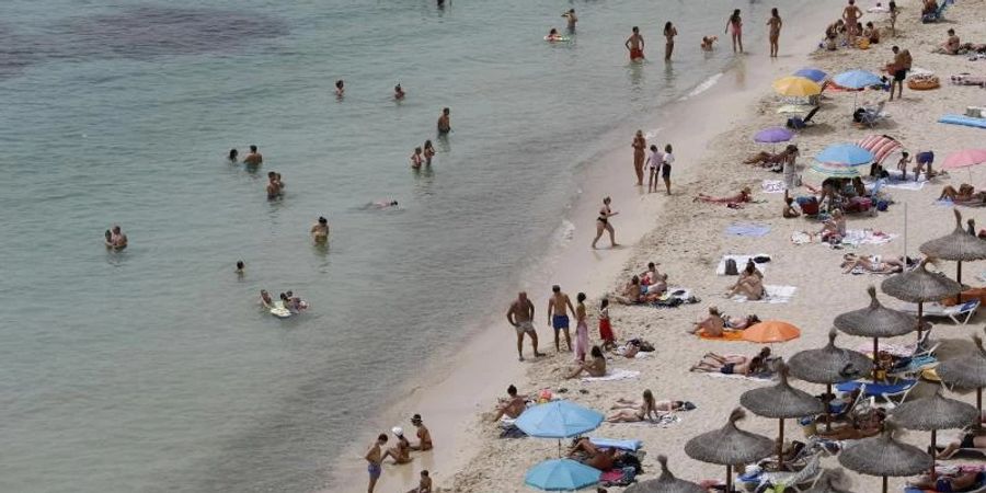 Touristen geniessen an einem Strand bei Puerto Portals auf Mallorca die Sonne und das Meer. Foto: Clara Margais/dpa