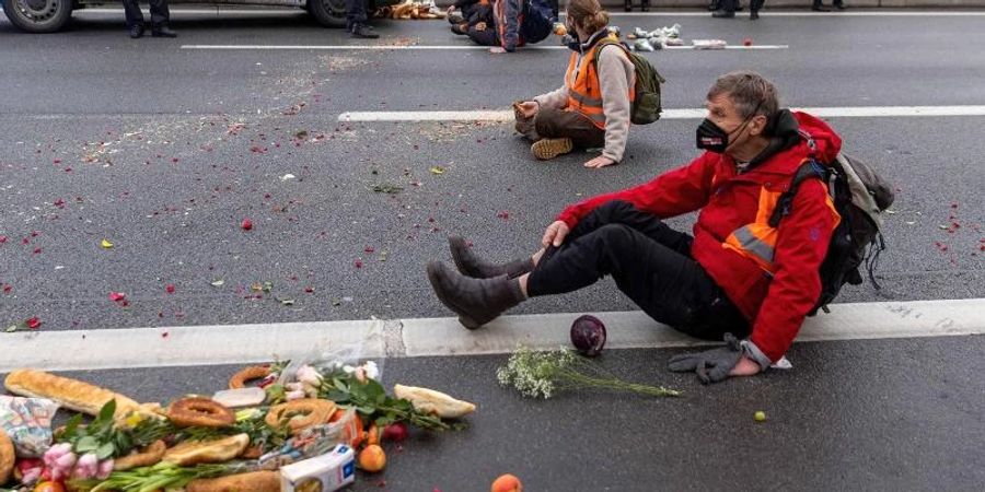 Klimaaktivisten der Gruppe «Aufstand der letzten Generation» sitzen auf der Fahrbahn und blockieren den Verkehr. Foto: Carsten Koall/dpa