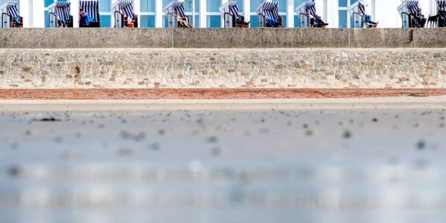 Touristen geniessen die Sonne in Strandkörben auf der Strandpromenade am Weststrand auf Norderney. Foto: Hauke-Christian Dittrich