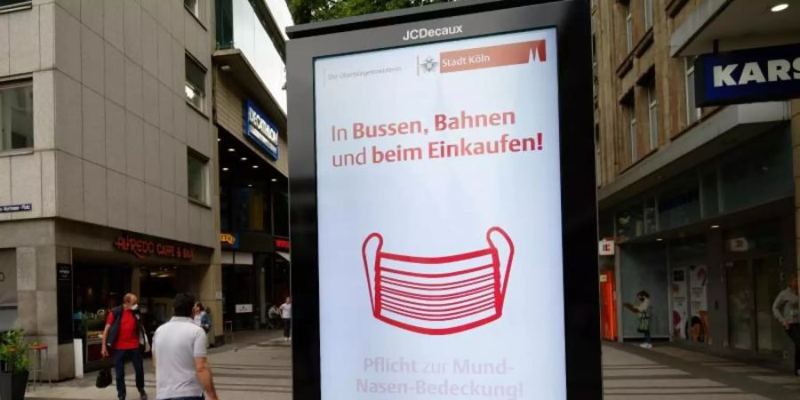 Ein Werbebildschirm weist in der Kölner Innenstadt auf die Maskenpflicht in Geschäften und im Nahverkehr hin. Foto: Henning Kaiser/dpa