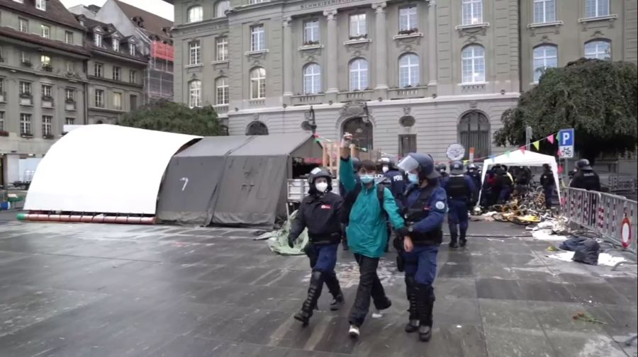 Einer der abgeführten Aktivisten streckt siegesreich die Faust in die Höhe.