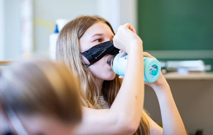 Eine Schülerin hebt ihre Mund- und Nasenmaske an um etwas zu trinken. (Symbolbild) Masken im Unterricht