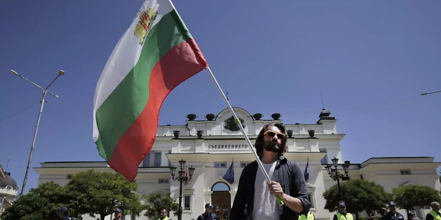 Ein Mann hält während einer Protestaktion vor dem bulgarischen Parlament die Fahne des Landes. Foto: Valentina Petrova/AP/dpa
