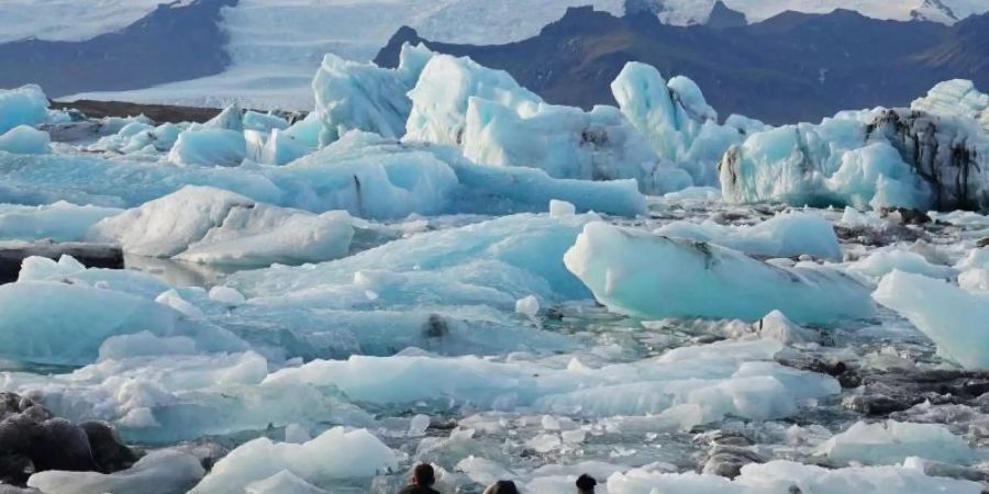 Touristen stehen vor Eisbergen in der Gletscherlagune Jökulsarlon im Süden Islands. Foto: Owen Humphreys/PA Wire/dpa