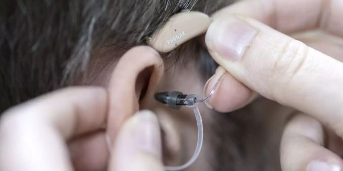 Ein Hörgerät wird in ein Ohr eingesetzt (Symbolbild) Coronavirus Symptom