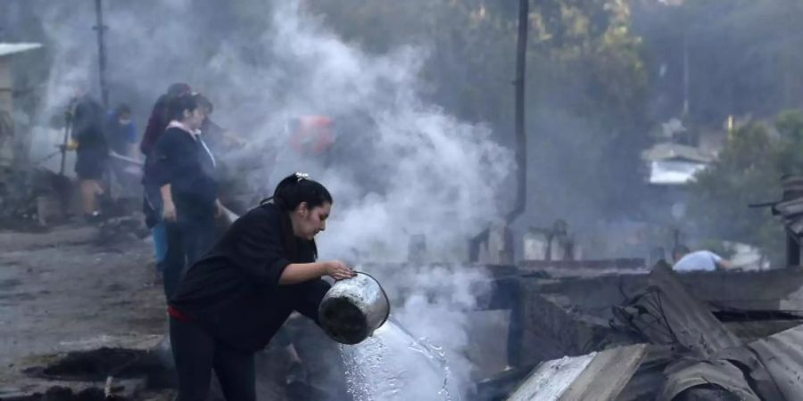 Einwohner schütten Wasser auf die qualmenden Überreste ihrer Häuser, die bei einem Brand zerstört wurden. Foto: Raul Zamora/Aton Chile/dpa