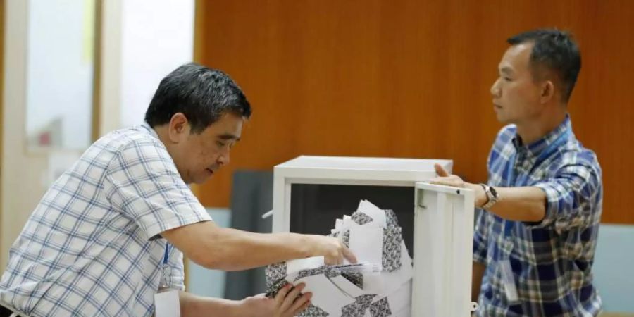 Helfer leeren eine Wahlurne. Foto: Vincent Thian/AP/dpa