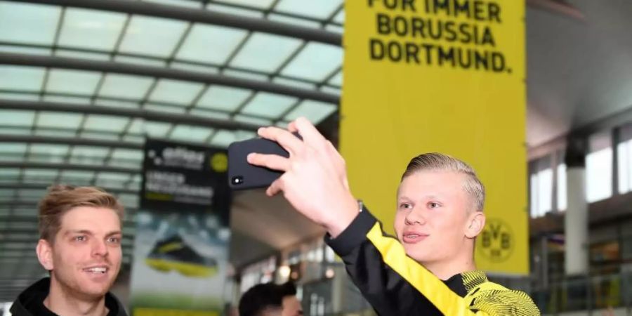 Erling Haaland (r) macht am Dortmunder Flughafen mit seinem Handy ein Selfie von sich. Foto: David Inderlied/dpa