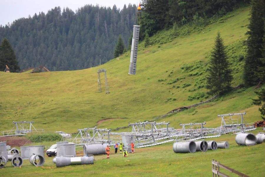 Bauarbeiter beobachten am 08.07.19, wie der Heliswiss Super Puma mit einem Mastenteil davonfliegt.