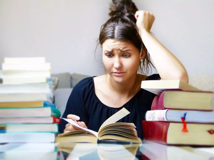 Eine Studentin sitzt vor einem Haufen Bücher. Bücher