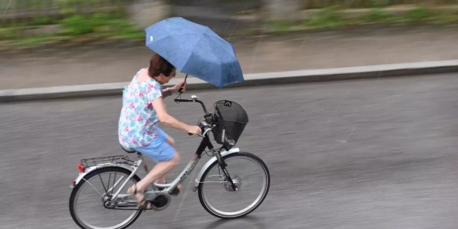 Mit einem Regenschirm trotzt eine Radfahrerin im bayerischen Garmisch-Partenkirchen dem Regen. Foto: Angelika Warmuth