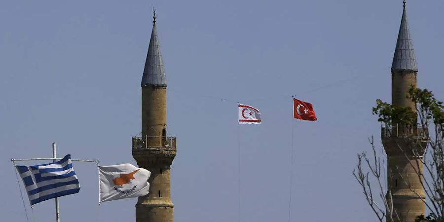 Griechische und zypriotische Flaggen flattern im Wind im südlichen Teil. Währenddessen im Norden, im türkisch besetzten Gebiet, eine türkische und eine türkisch-zypriotische Flagge auf einem Minarett der Selimiye-Moschee in der geteilten Hauptstadt Zyperns wehen. Foto: Petros Karadjias/AP/dpa