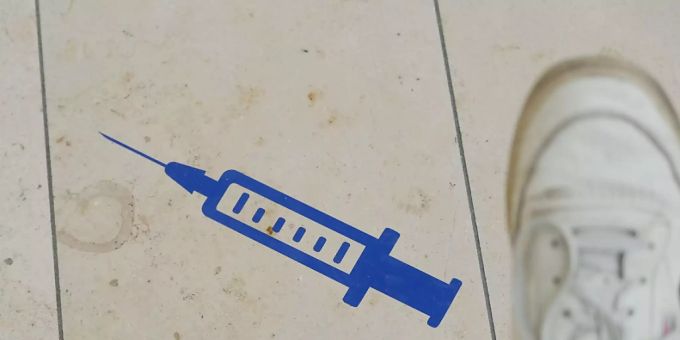 ARCHIV - Das Symbol einer Spritze ist auf dem Boden der Muldentalhalle in Sachsen aufgeklebt. Foto: Sebastian Willnow/dpa-Zentralbild/dpa Corona-Impfung