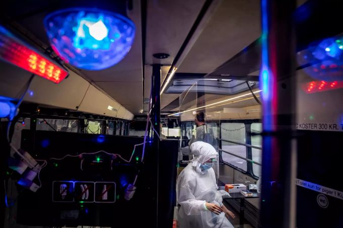 dpatopbilder - 23.02.2021, Dänemark, Ishoej: Eine Frau in Schutzausrüstung sitzt in einer mobilen Corona-Teststation in einem Bus. Disco-Beleuchtung und Musik sollen den Besuchern im Bus die Zeit angenehmer gestalten, während sie getestet werden. Foto: Mads Claus Rasmussen/Ritzau Scanpix/AP/dpa +++ dpa-Bildfunk +++ Coronavirus - Dänemark