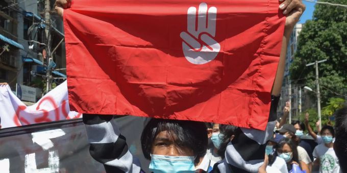 11.05.2021, Myanmar, Yangon: Ein Protestteilnehmer hält während einer Demonstration eine Fahne hoch, auf der das Drei-Finger-Zeichen des Widerstandes zu sehen ist. Protest gegen Militärjunta in Myanmar