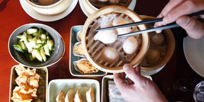 Ein Mann greift mit Essstäbchen nach Dim sum, gedämpften Teigtaschen, in einem Bambuskorb. Ein Mann greift mit Essstäbchen nach Dim sum, gedämpften Teigtaschen, in einem Bambuskorb.