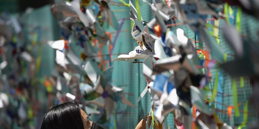 Eine Frau hängt während einer Gedenkveranstaltung Stecknadelräder im Gedenken an Corona-Opfer an eine Wand in Sao Paulo. (Archivbild) Foto: Andre Penner/AP/dpa