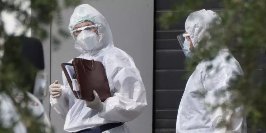 Medizinische Mitarbeiter in Schutzkleidung unterhalten sich, während sie einen Patienten mit Verdacht auf eine Coronavirus-Erkrankung in einem Krankenhaus transportieren. Die russische Hauptstadt Moskau verzeichnet weiterhin Tausende Corona-Neuinfektionen. Foto: Pavel Golovkin/AP/dpa