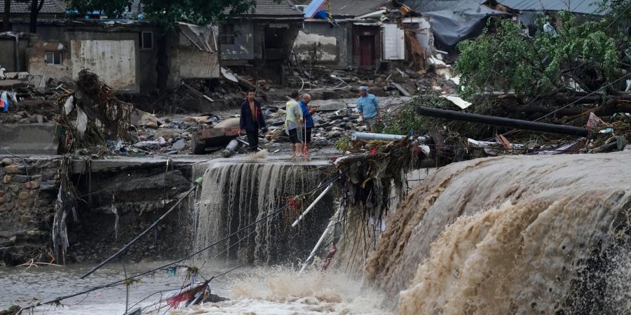 Menschen stehen in Peking vor von den Wassermengen zerstörten Häusern. Die extremen Regenfälle sind eine Folge des Tropensturms «Doksuri».