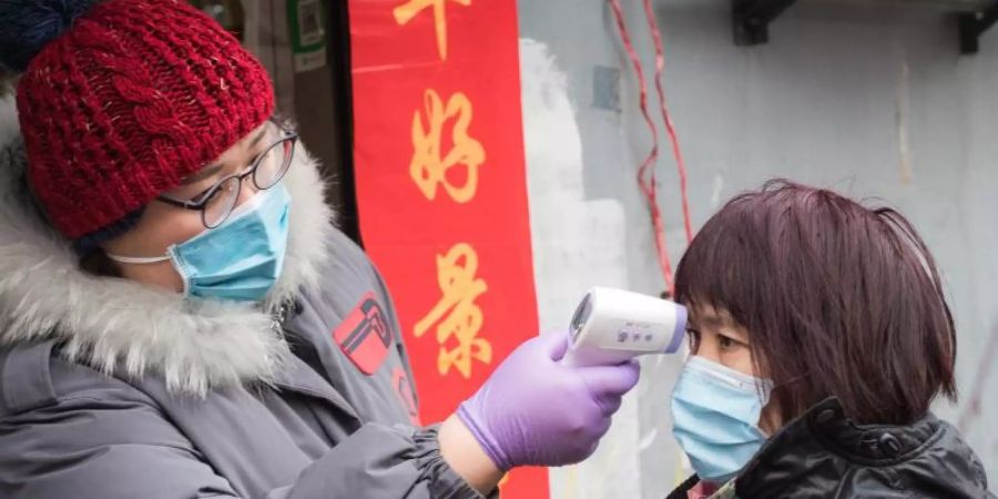 Eine Gemeindemitarbeiterin misst die Körpertemperatur einer Passantin in der Nähe der Kranichpagode in Wuhan. Foto: Xiao Yijiu/XinHua/dpa