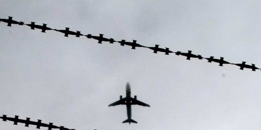 ARCHIV - Ein Flugzeug ist hinter Stacheldraht zu sehen. Foto: Julian Stratenschulte/dpa