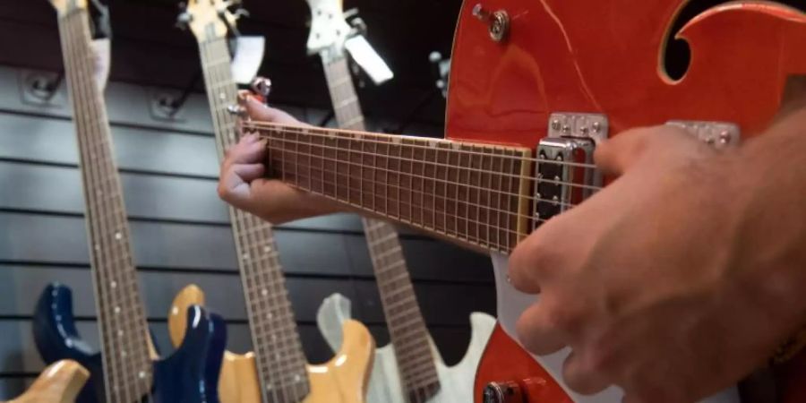 Ein Mann spielt in einem Gitarrenladen auf einer Linkshänder-Guitarre. Foto: Paul Zinken/dpa