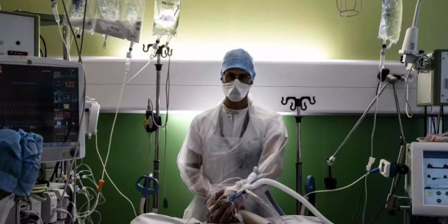 Ein medizinischer Angestellter (M) kümmert sich auf der Intensivstation eines Krankenhauses in Pierre-Benite um einen Corona-Patienten. Foto: Jeff Pachoud/AFP/dpa