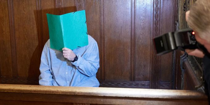 Der Angeklagte sitzt im Landgericht Berlin und verbirgt sein Gesicht hinter einem Schnellhefter. Angeklagter vor Gericht