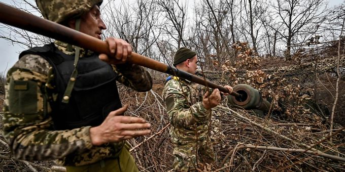Zwei Soldaten reinigen das Rohr einer getarnten selbstfahrenden Panzerhaubitze. russland ukraine krieg