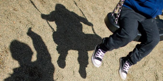 Der Schatten von einem Mann und einem schaukelnden Kind auf einem Spielplatz. pädophil