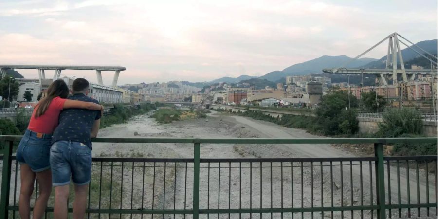 Ein Paar steht auf einer Brücke, von der man auf die Überreste des Polcevera-Viadukts (Morandi-Brücke) in Genua (IT) sehen kann.