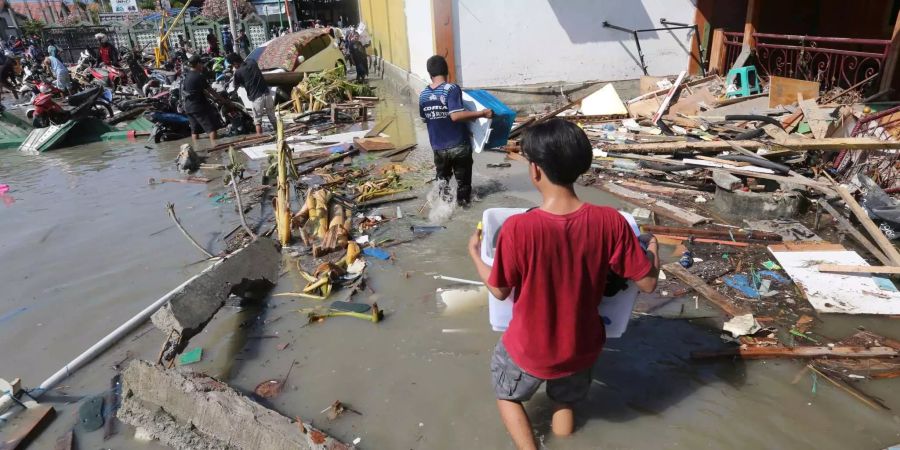 Menschen tragen Gegenstände von einem beschädigten Einkaufszentrum in Palu, Zentral-Sulawesi, weg.