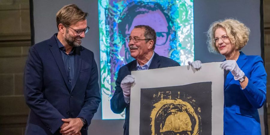 Jürgen Klopp (l-r), Fussballtrainer des FC Liverpool, Peter Krawietz, ehemaliger Mainzer Kulturdezernent und Mitglied der Preisfindungskommission und Annette Ludwig, Direktorin des Gutenberg-Museums Mainz, stehen mit der goldenen Druckgrafik mit dem Porträt des Fussballtrainers auf der Bühne.