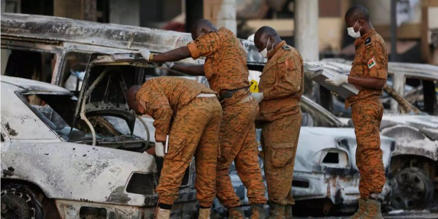 Mehrere Soldaten schauen sich in Burkina Faso ein ausgebranntes Auto an.