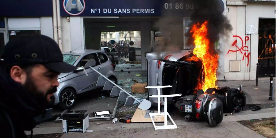 Ein Mann geht an angezündeten Auto und Roller während der Demonstration zum 1. Mai vorüber.