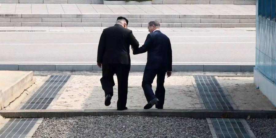 Kim Jong-un (l), Machthaber von Nordkorea, und Moon Jae In, Präsident von Südkorea, gehen Hand in Hand über die Betonschwelle, die die Grenze zwischen ihren Ländern markiert nach Nordkorea.