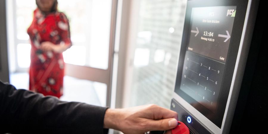 Ein Mitarbeiter hält für die Arbeitszeiterfassung seinen Chip an einen Zeiterfassungsterminal.