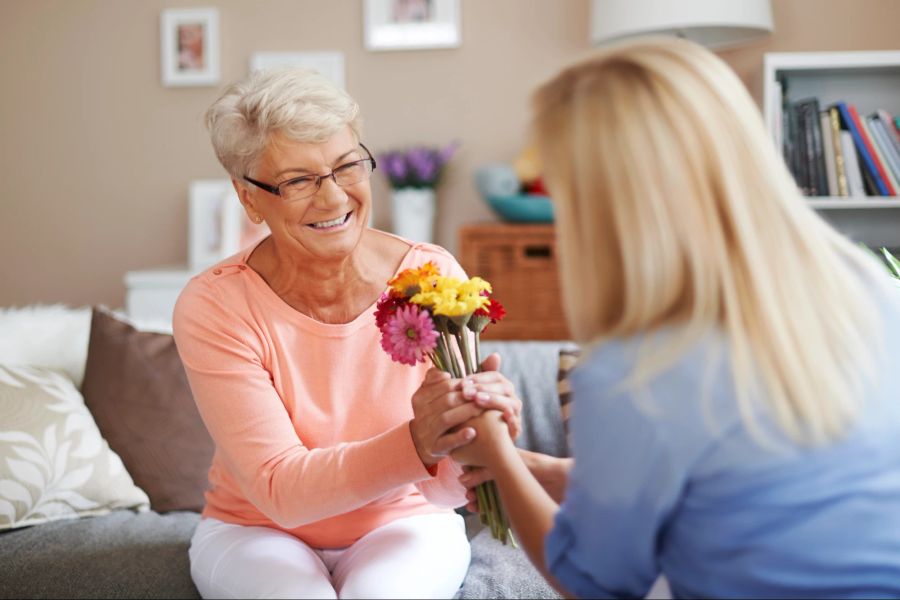 Frau übergibt Seniorin Blumenstrauss