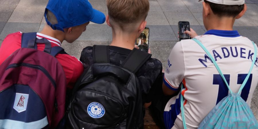 Hugo W., (r-l), Hardy M. und Edan A., alle 11 Jahre alt, benutzen ihre Telefone, während sie vor einer Schule in Sydney sitzen. In Australien dürfen ab sofort Kinder und Jugendliche u...
