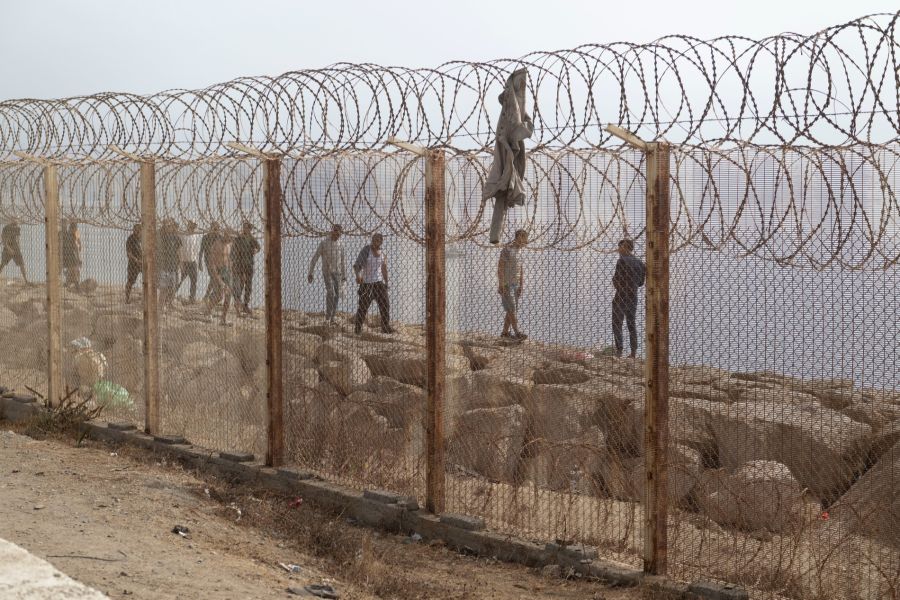 Migranten balancieren auf den Felsen entlang des mit Stacheldraht gesicherten Grenzzauns zwischen Marokko und Ceuta.