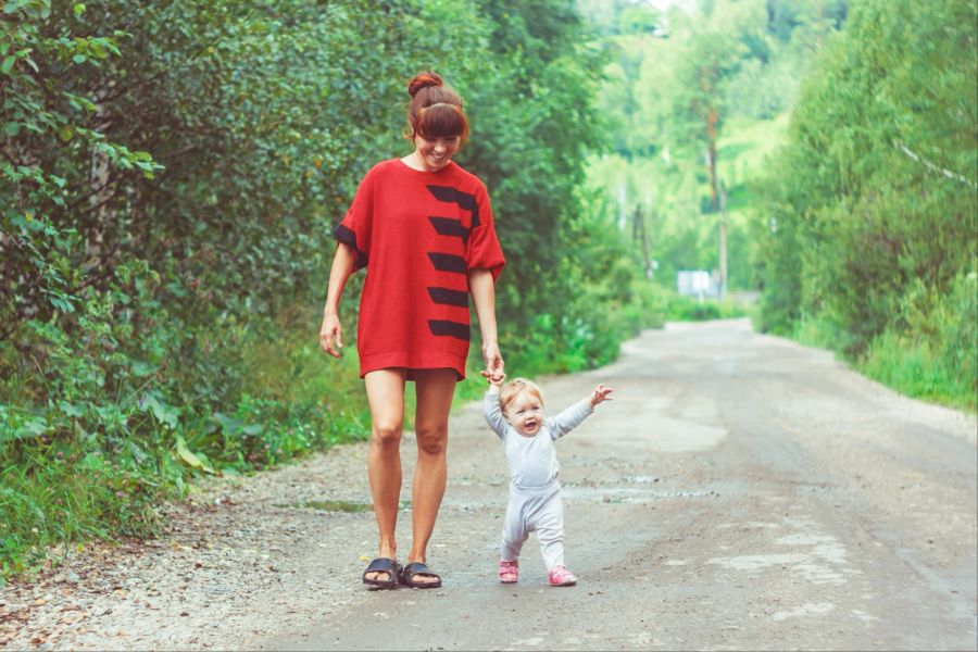 Kind lernt Laufen im Freien an der Hand der Mutter.