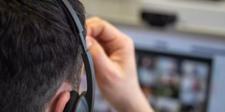 Ein junger Mann, der ein Headset trägt, nimmt an einer Videokonferenz teil. Foto: Sebastian Gollnow/dpa