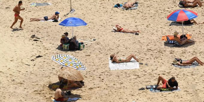 Menschen sonnen sich während der Hitzewelle am Strand des Bondi Beach und halten dabei Abstand zueinander. Meteorologie