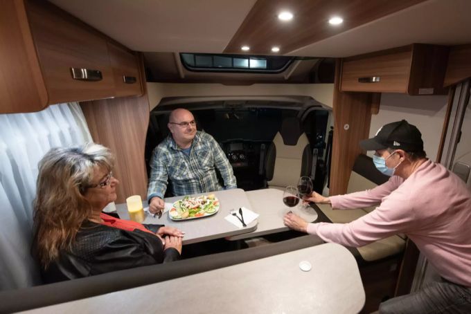 Der Betreiber eines Restaurants bedient zwei Wohnmobilisten in ihrem Wohnwagen. Wohnmobil dinner