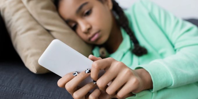 Cybermobbing hinterlässt oft seelische Narben bei Kindern und Jugendlichen. Trauriges Mädchen liegt auf dem Sofa mit Smartphone