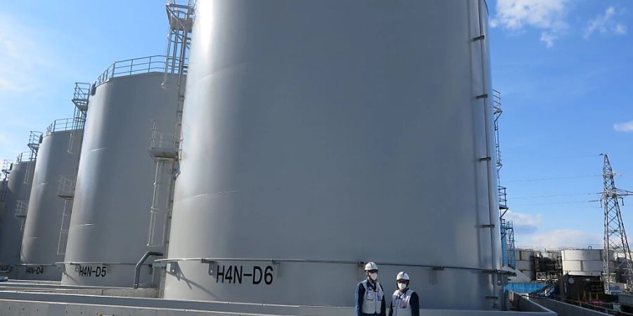 ARCHIV - Zwei Mitarbeiter des Betreiberkonzerns Tepco stehen vor riesigen Tanks, in denen verstrahltes Wasser, das bei der andauernden Kühlung der beschädigten Reaktoren von Fukushima anfällt, gelagert wird. Foto: Lars Nicolaysen/dpa