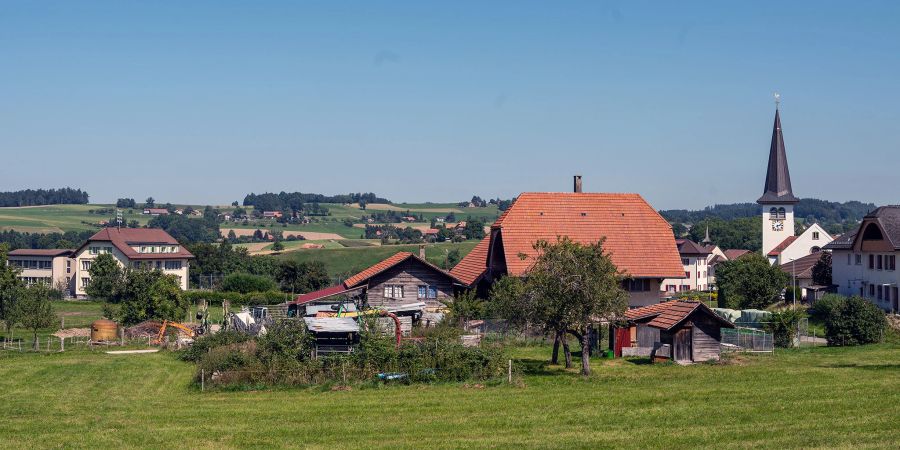 Blick auf das Dorf St. Ursen mit dem Schulhaus links und der katholischen Kirche rechts.