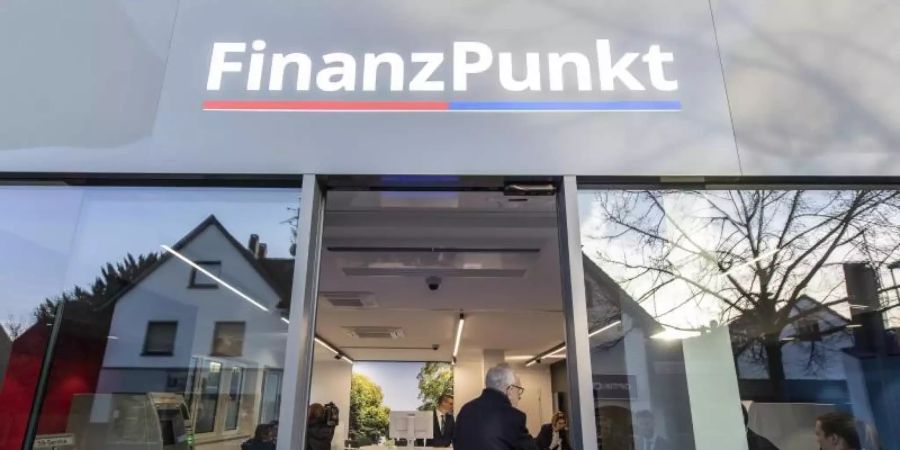Besucher stehen zur Eröffnung vor dem «Finanzpunkt». In der Bankfiliale kooperieren die Taunus Sparkasse und die Frankfurter Volksbank. Foto: Boris Roessler/dpa