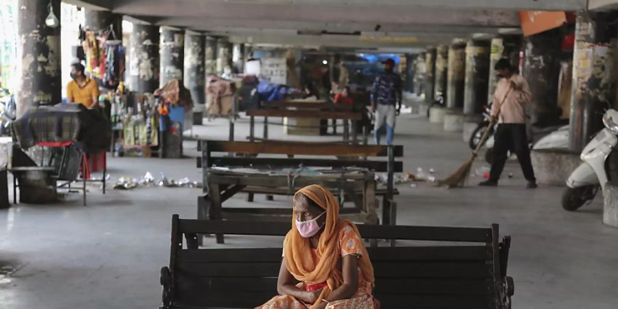 Eine Frau trägt eine Schutzmaske und wartet an einem verlassenen Busbahnhof. (Archivbild) Foto: Channi Anand/AP/dpa